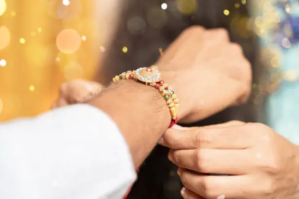 Closeup of hands, sister tying rakhi, Raksha bandhan to brother's wrist during festival or ceremony - Rakshabandhan celebrated across India as selfless love or relationship between brother and sister.