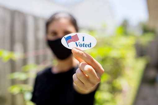 Young woman wearing face mask holding I voted today sticker.