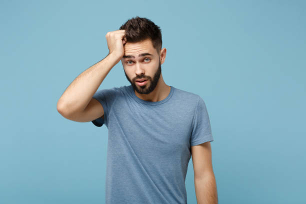 istock Young exhausted sick man in casual clothes posing isolated on blue wall background, studio portrait. People sincere emotions lifestyle concept. Mock up copy space. Putting hand on head looking camera. 1258006899