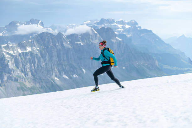 le coureur de sentier femelle traverse la crête neigeuse de montagne - cross coat photos et images de collection