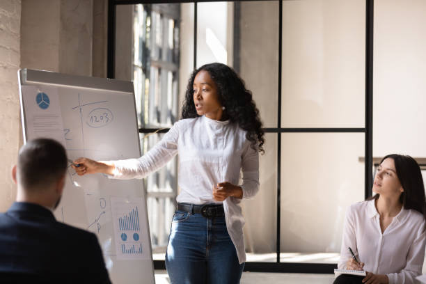 African American female coach present project on whiteboard Young African American female coach or speaker make whiteboard presentation for diverse employees in office, focused biracial woman trainer present business project on flip chart at meeting whiteboard visual aid stock pictures, royalty-free photos & images