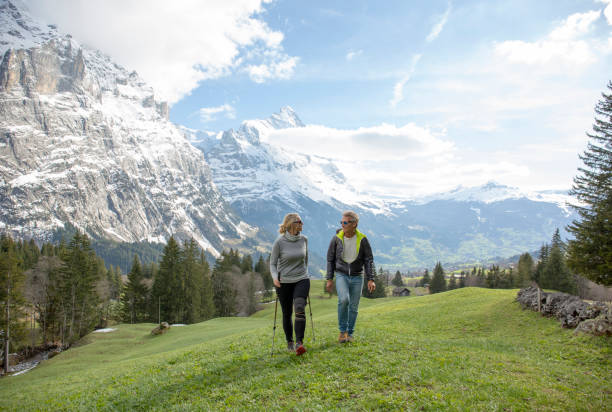 Hiking couple walk through grassy meadow in spring Swiss alps in background grindelwald photos stock pictures, royalty-free photos & images