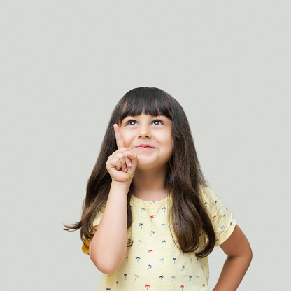 Portrait of serious funny little girl looking at camera on grey background
