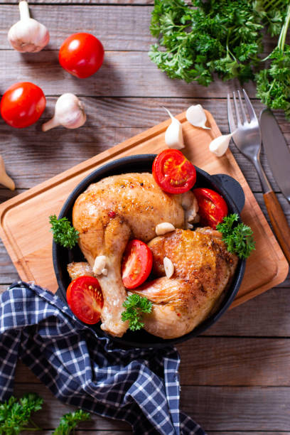 istock Hot chicken legs with basil and tomatoes served in a frying pan on table. Top view, vertical. 1258017113