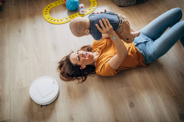istock Young mother playing with her little boy while robotic vacuum cleaner cleaning 1258021774