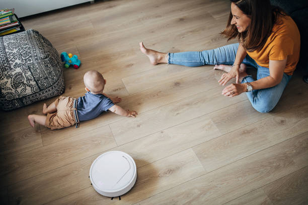 istock Young mother playing with her baby son while robotic vacuum cleaner cleaning 1258021831