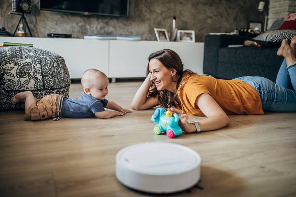 istock Mother playing with her baby boy while robotic vacuum cleaner cleaning floor 1258024032