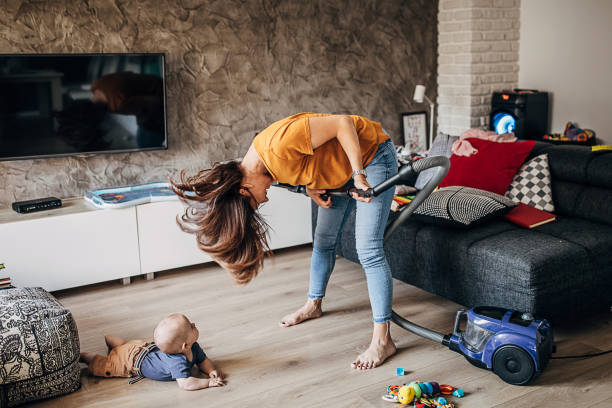 cheerful young mother having fun with her baby boy while vacuuming - spring cleaning women cleaning dancing imagens e fotografias de stock