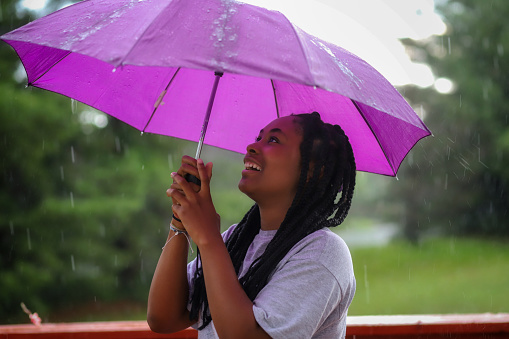 A portrait of a beautiful African-American teenaged girl holding a umbrella outside in the rain and smiling