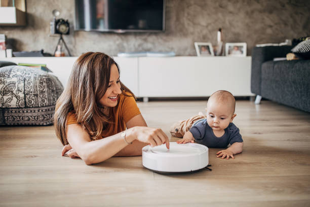 istock Cheerful mother playing with her baby boy while robotic vacuum cleaner cleaning 1258025030