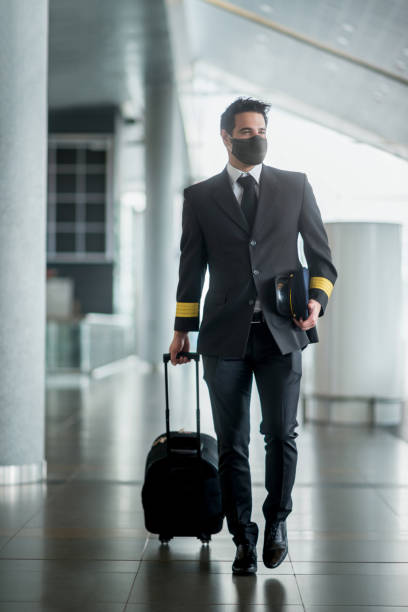 フェイスマスクを着用して空港を歩き、バッグを持っているパイロット - cabin crew pilot airport walking ストックフォトと画像