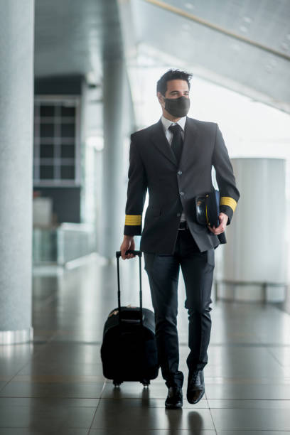 pilot walking at the airport wearing a facemask and carrying his bag - cabin crew pilot airport walking imagens e fotografias de stock