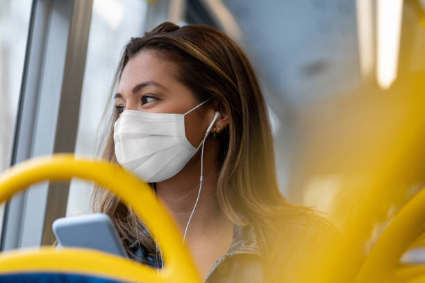 femme montant sur un bus utilisant un masque facial et écoutant la musique avec des écouteurs - london england audio photos et images de collection