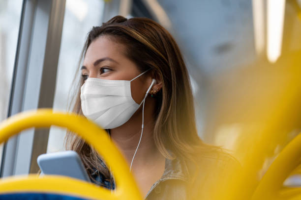 Woman riding on a bus wearing a facemask and listening to music with headphones Portrait of a woman riding on a bus wearing a facemask and listening to music with headphones â public transport during the COVID-19 pandemic window seat vehicle stock pictures, royalty-free photos & images