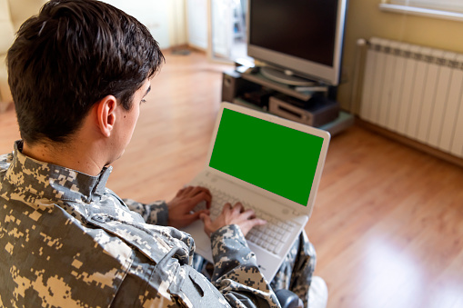 A retired soldier in a wheelchair with physical disabilities is sitting in his living room and feeling lonely while communicating with his family over his laptop.