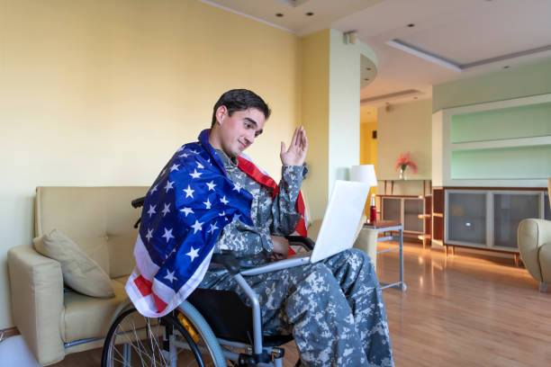 istock Retired Soldier With Physical Disabilities is Using a Laptop and Holding US Flag 1258035719