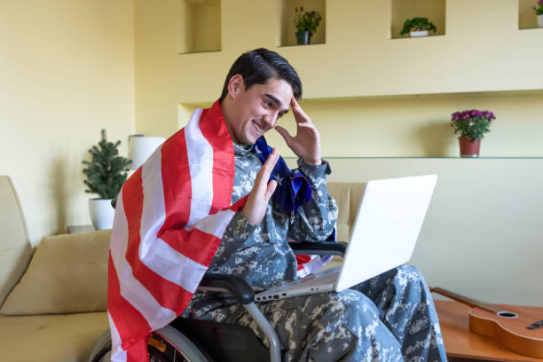 istock Retired Soldier With Physical Disabilities is Using a Laptop and Holding US Flag 1258035728