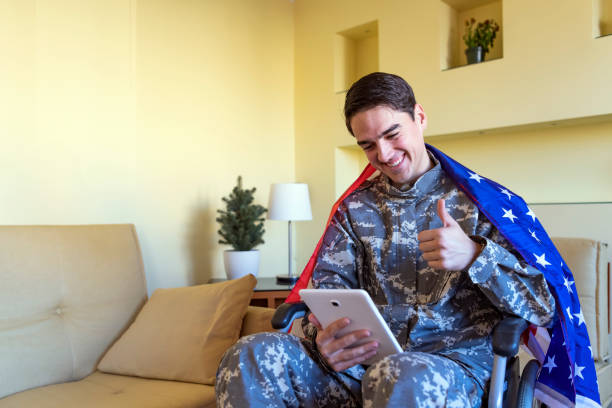 istock Young War Veteran is Communicating over the Digital Tablet and Holding a US Flag 1258035757