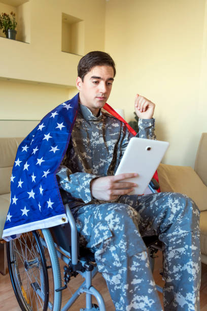 istock Young War Veteran is Communicating over the Digital Tablet and Holding a US Flag 1258036350