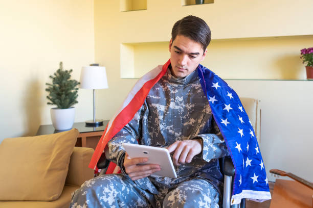 istock Young War Veteran is Communicating over the Digital Tablet and Holding a US Flag 1258036378