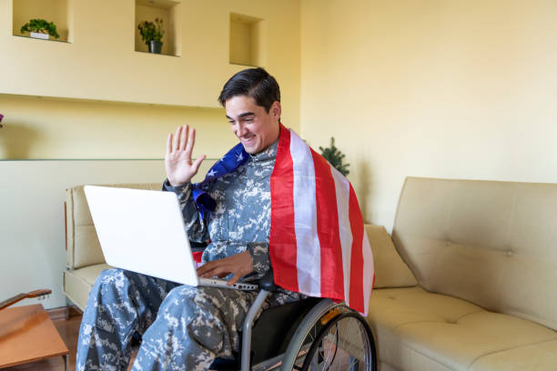 istock Retired Soldier With Physical Disabilities is Using a Laptop and Holding US Flag 1258036421