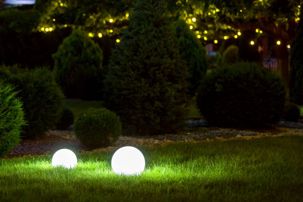 istock backyard ground light garden with lantern electric lamp with sphere diffuser in green grass and garland bublb on thuja bushes with stone mulching in park with landscaping, closeup night scene nobody. 1258037298