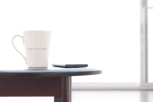 white ceramic coffee cup and smart phone on oval wooden table with blurred frosted glass sliding door in white living room Close up white ceramic coffee cup and smart phone on oval wooden table with blurred frosted glass sliding door in white living room frosted glass door office stock pictures, royalty-free photos & images