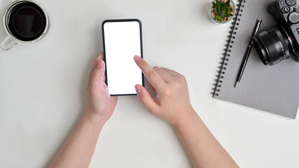 istock hand businesswoman using a telephone, blank screen smart phone, notebook, camera and coffee cup on white table top view. 1258065907