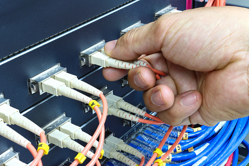 Technician connect fiber cable network to switch port in server room , Concept internet network management