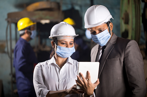 Businessman and businesswoman with protective face mask using digital tablet at factory