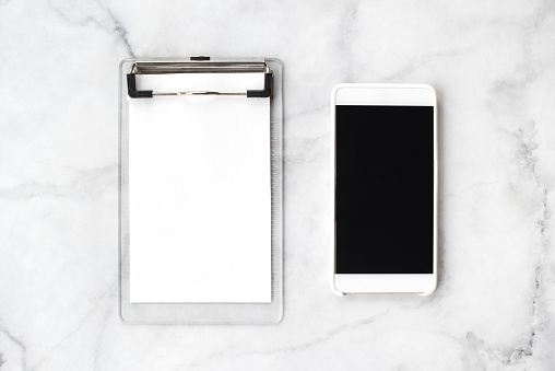 Cellphone with black screen and blank notebook on marble background. Modern office and work concept. Top view, flat lay.