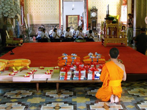 joven monje budista arrodillado ante las ofrendas recibidas en el templo wat benchamabophit en bangkok, tailandia. - monk meditating thailand bangkok fotografías e imágenes de stock