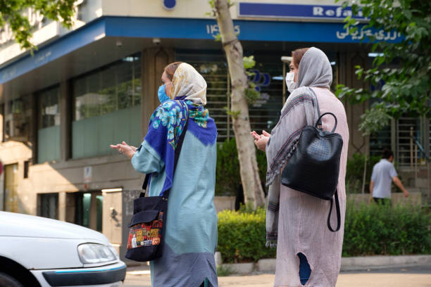 Iranian women following Covid-19 protective protocols This is a street in Tehran. Two Iranian women in hijab and protective masks are crossing the street while using hand sanitizer. These are the basic protective protocols in the time of coronavirus pandemic. tehran stock pictures, royalty-free photos & images