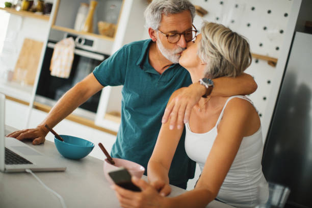 Love and work in the morning. Mature couple has breakfast and finishes some work from home. A short break for a kiss. kissing on the mouth stock pictures, royalty-free photos & images