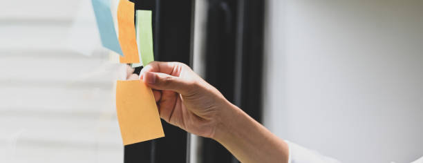 istock Cropped image a hand is holding an empty sticky note at the glass wall. 1258086139