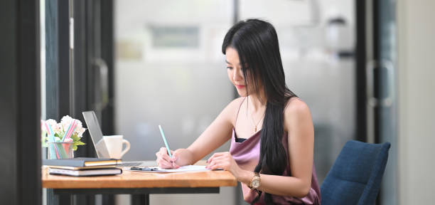 istock A beautiful woman is taking notes at the wooden working table. 1258086278
