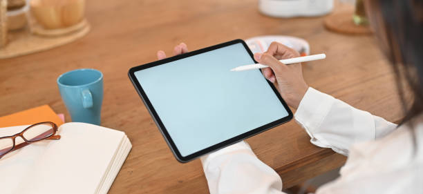 istock Cropped image of a woman's hands is using a white blank screen computer tablet on the wooden table. 1258086343