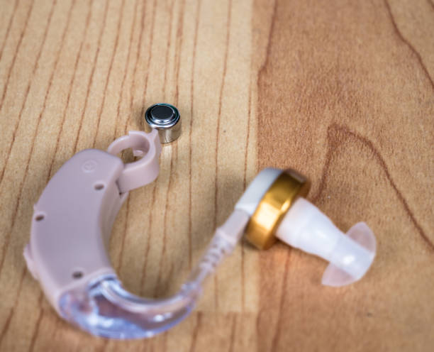 istock Hearing aid with open battery holder and a small battery on a wooden table. 1258091644