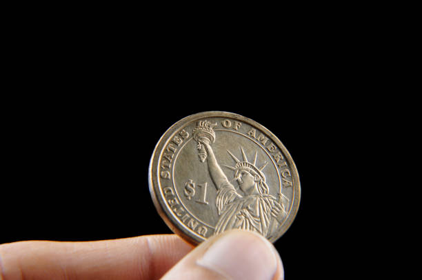 istock Hand holding one dollar coin  isolated on black 1258096429