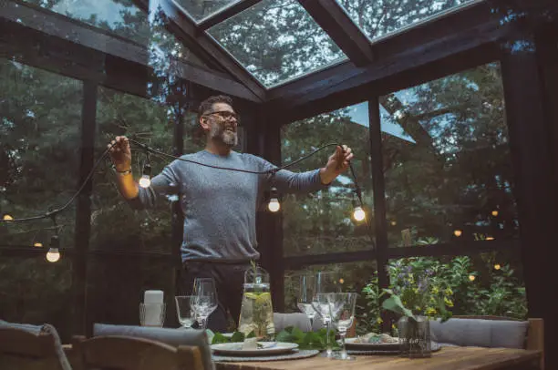 Mature men arranging table and greenhouse for cozy dinner with friends.