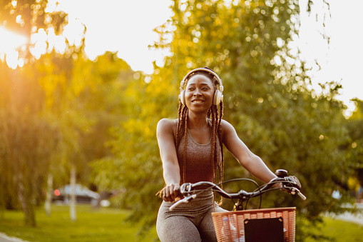 Photo of a young African American woman is on her bicycle using wireless headphones