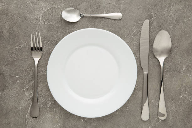 istock Table setting with white plates, and cutlery - fork, spoon and knife. Shot from above. Copy space on empty plate. 1258112843