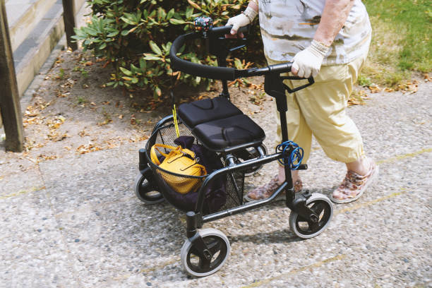elderly woman walking outside with rollator or wheeled walker - authentic real people concept
