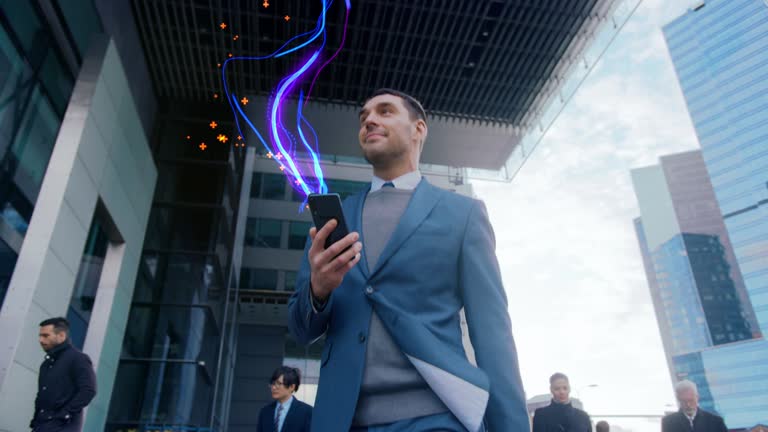 Handsome Businessman Uses Smartphone with Animated Abstract Digital Data Lines Flying, Walks on Crowded City Streets. Big Data, Information, e-Business Concept. Low Angle Front View Following Shot