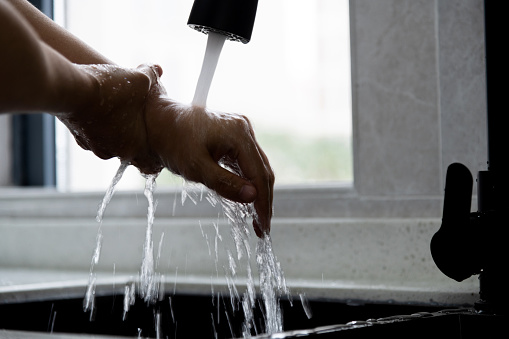 Woman washing hands under running water in the kitchen.