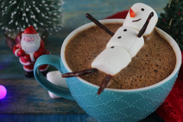 istock Image of group of objects, model Christmas trees, mug hot chocolate drink / cocoa with marshmallow snowman, Father Christmas figurine, string fairy light decoration, red and white Santa hat and marshmallows, turquoise tongue groove effect backdrop 1258116986