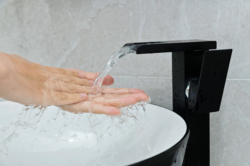Woman washing hands under running water in the bathroom.