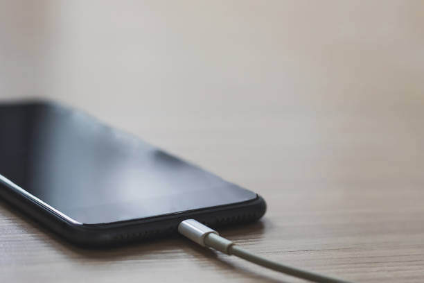 istock Mobile smart phones charging on wooden table background 1258120079