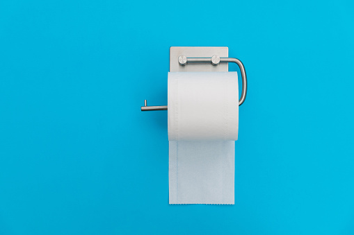 Roll of white toilet paper hanging on blue background.