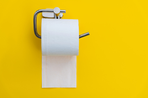 Roll of white toilet paper hanging on yellow background.